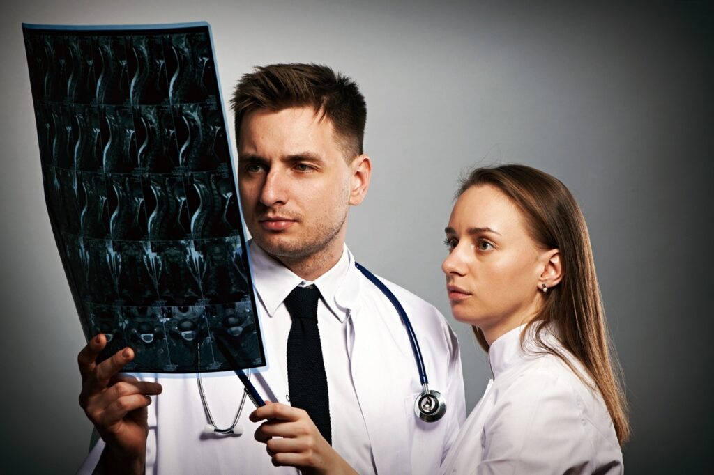Two medical professionals examining spinal MRI scans, focusing on images of the cervical spine.