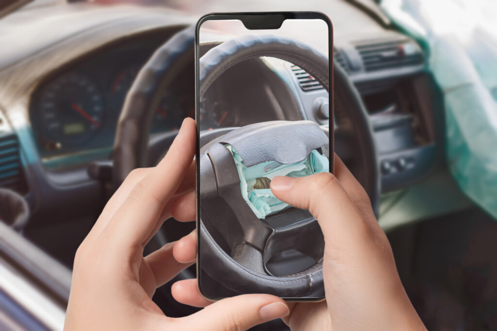 Hands holding a smartphone taking a photo of a steering wheel with a deployed airbag after a car accident.