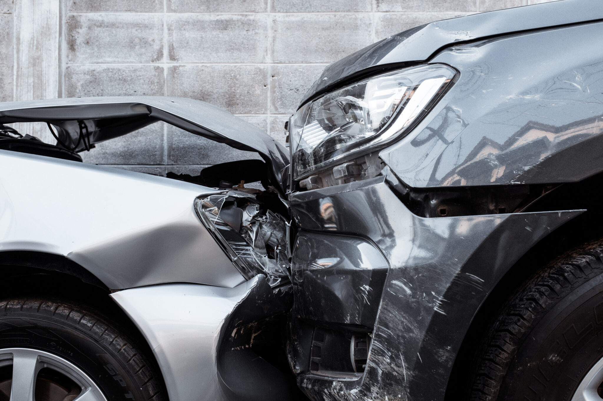 Close-up of the front ends of two damaged cars after a collision, showing crumpled hoods, broken headlights, and scraped body panels.
