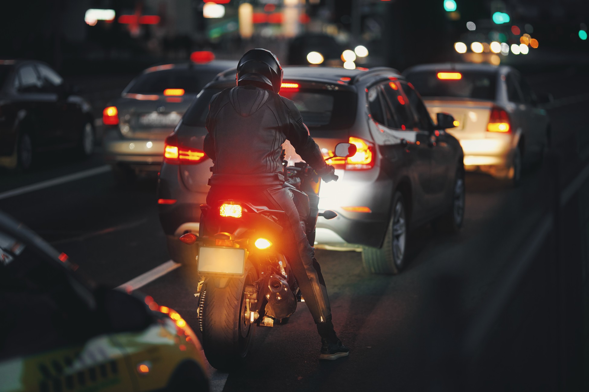 Motorcyclist stopped in heavy night traffic surrounded by car brake lights
