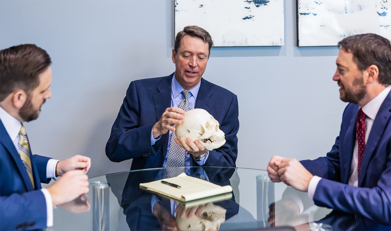 three lawyers sit at a table looking at a fake skull