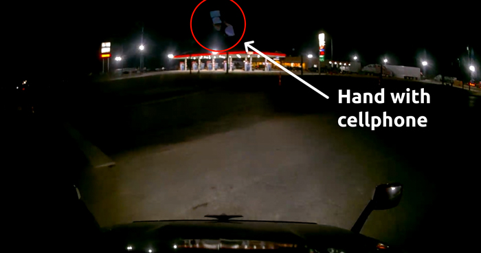 Dashcam view showing the reflection of a hand with a cellphone revealing distracted driving