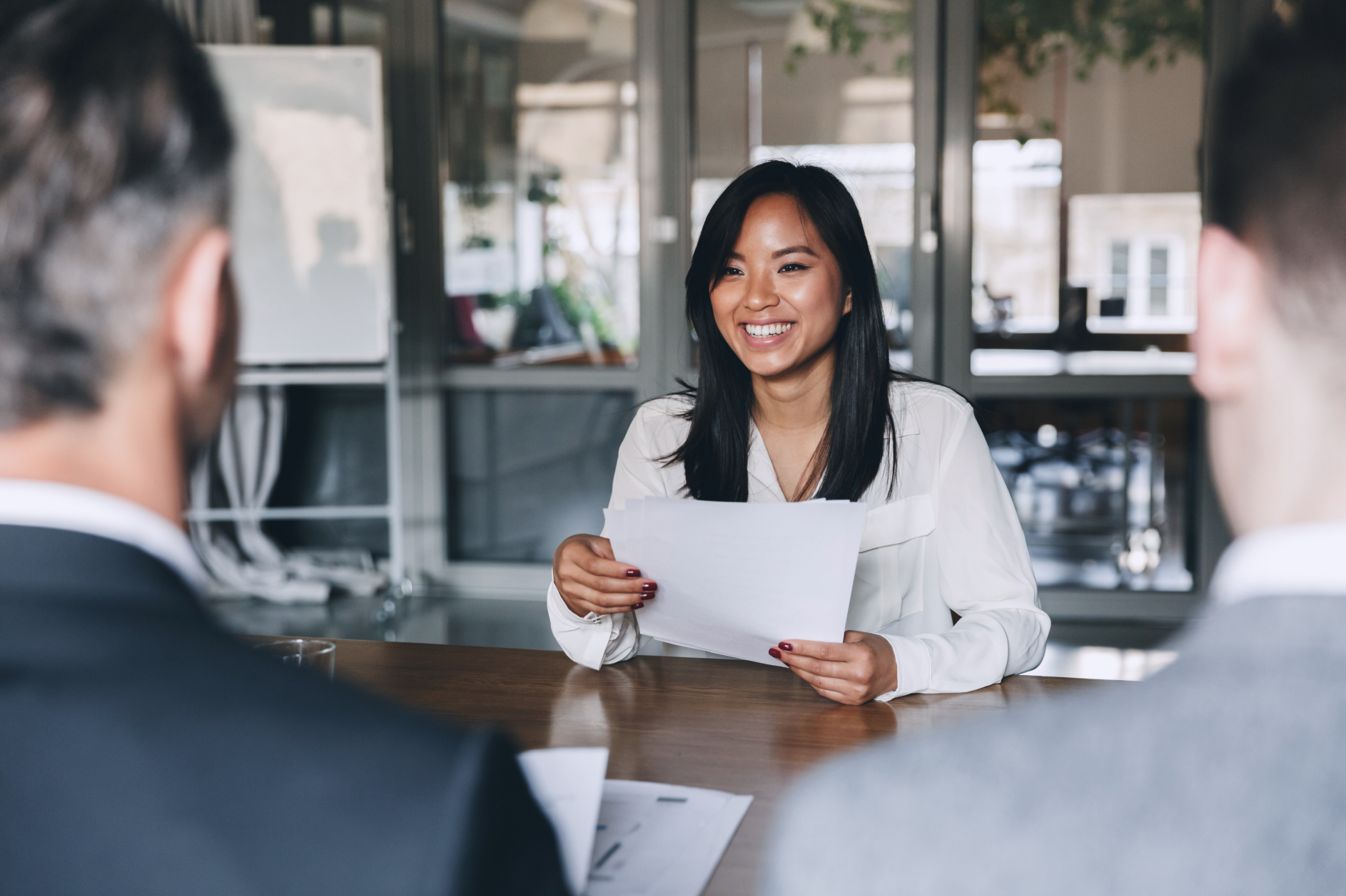Smiling woman holding papers across table in a meeting with two men.