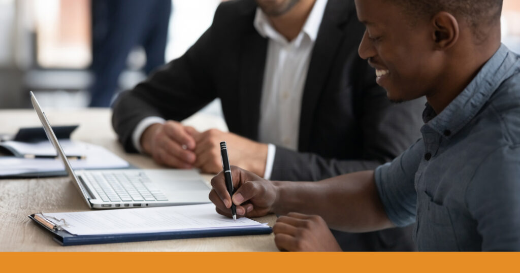 Smiling man sitting with an attorney signing legal documents.