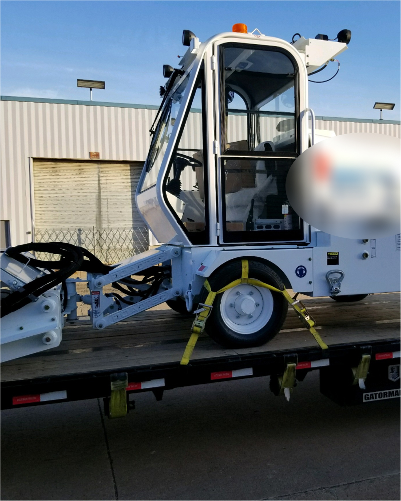 a white street sweeper on a flatbed