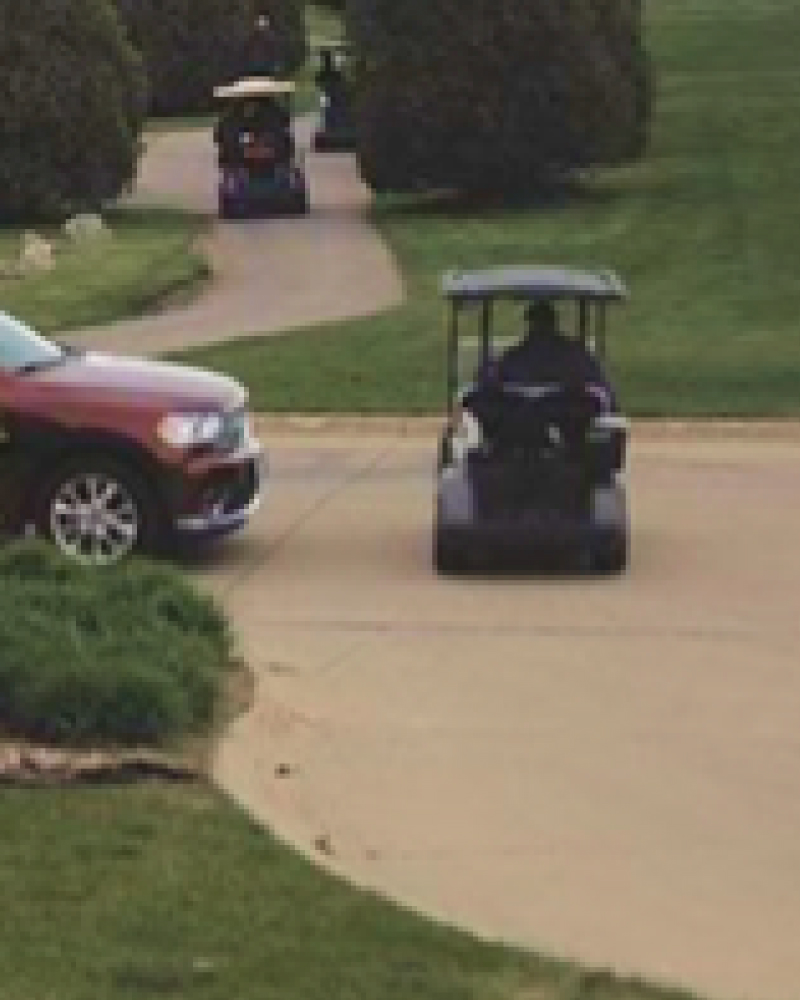 a golf cart driving across the street in front of a vehicle