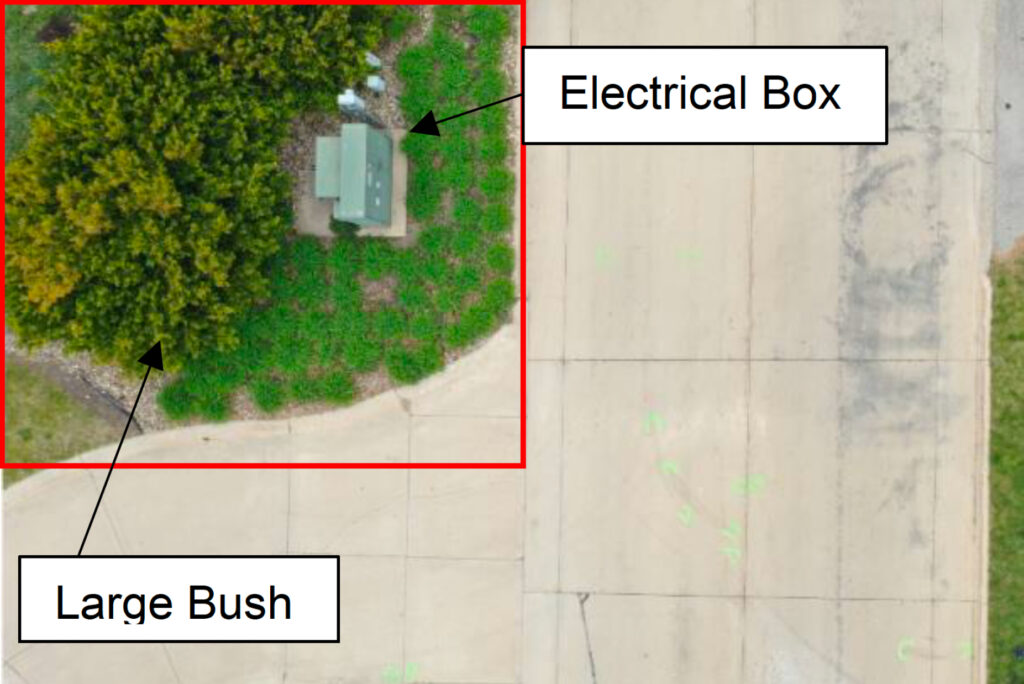 overhead view of a road and driveway with a bush and electrical box on the corner