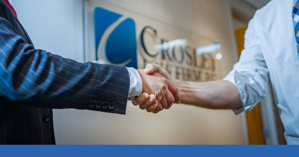 two people shaking hands in front of a Crosley Law Firm sign