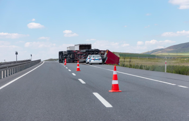 Scene of a highway accident involving an overturned semi-truck, with traffic cones and a police car blocking lanes for safety.