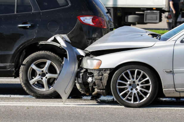 A silver sedan with severe front-end damage after crashing into the rear of a black SUV, showing a typical rear-end collision on the road.