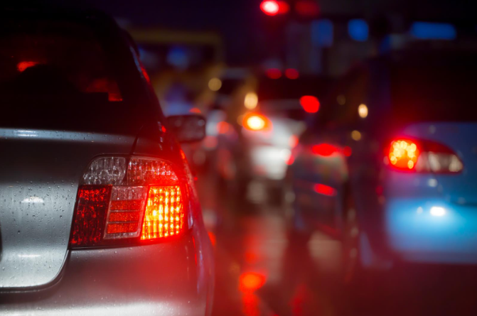 Cars stopped in heavy nighttime traffic on a wet road, with red brake lights reflecting on the pavement.