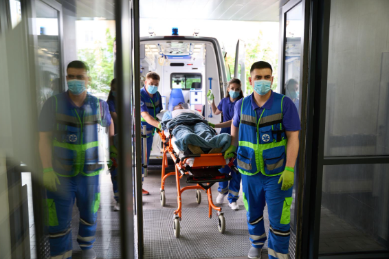 Paramedics wearing masks and safety vests wheel a patient on a stretcher into a hospital from an ambulance.