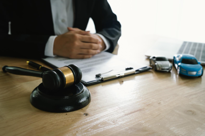 A lawyer sitting at a desk with a gavel, clipboard, and model cars, reviewing legal documents related to a car accident case.
