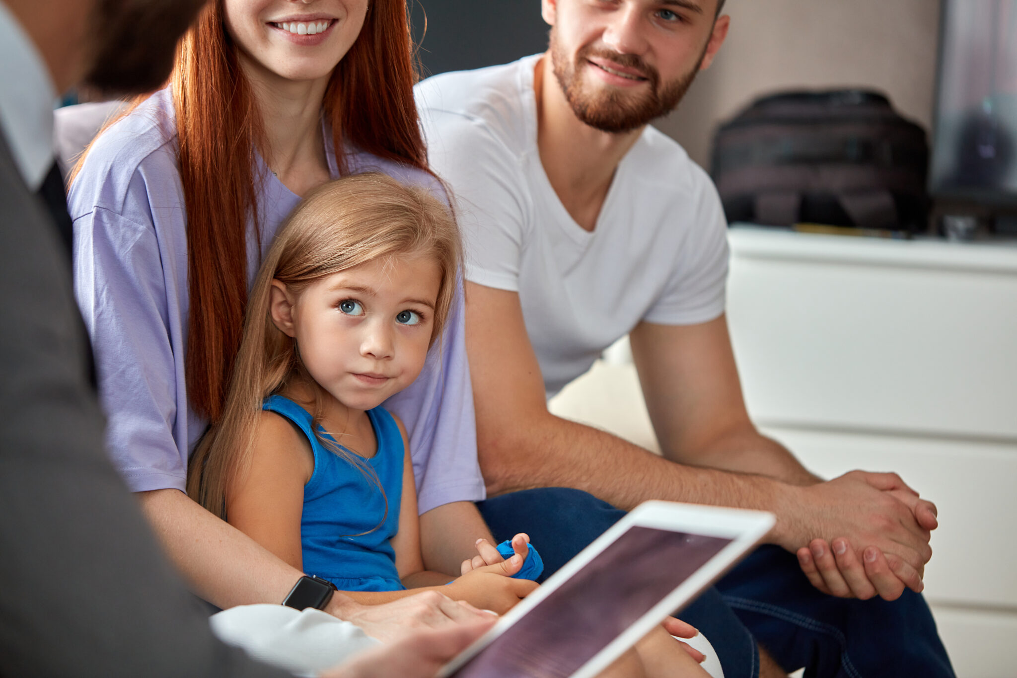 Young family with a child sitting together while speaking with a professional holding a tablet during a consultation.