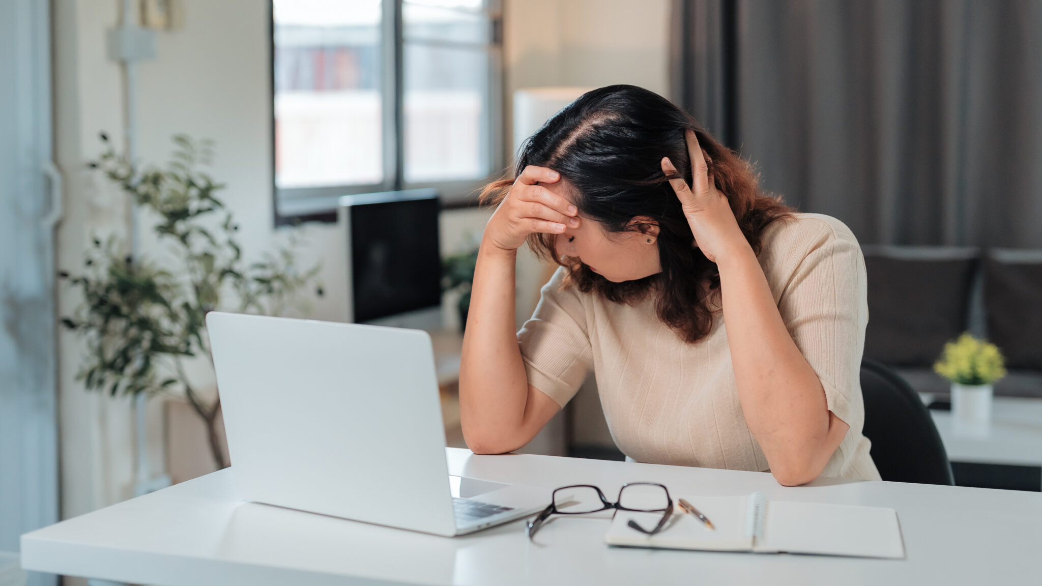 Woman feeling stressed and having a headache while sitting at a laptop computer, suffering from work burnout at home