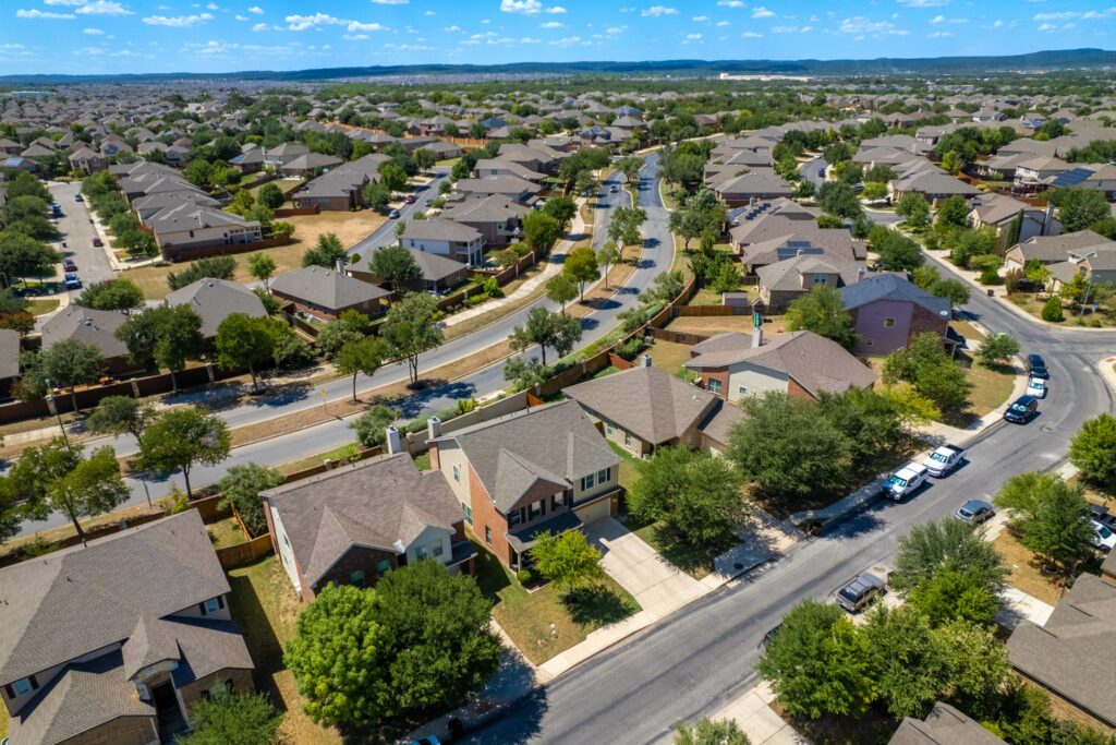 Aerial view of a suburban neighborhood with rows of houses and winding streets under a clear sky.