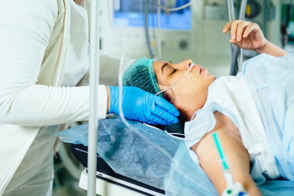 Patient lying on a hospital bed with an oxygen tube while a medical professional provides care.