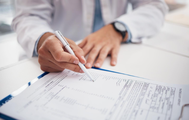 Person signing a document on a clipboard with a pen at a desk.