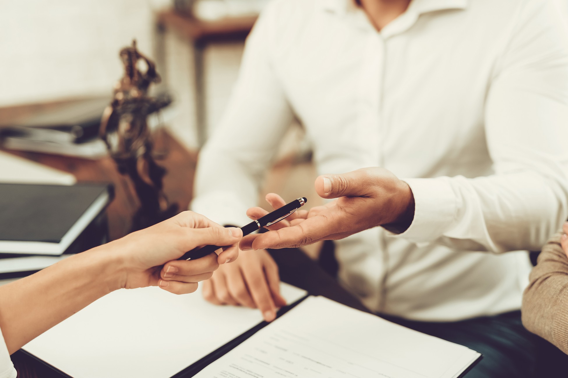 Close-up of a person handing a pen to another individual over a document, indicating signing or agreement.