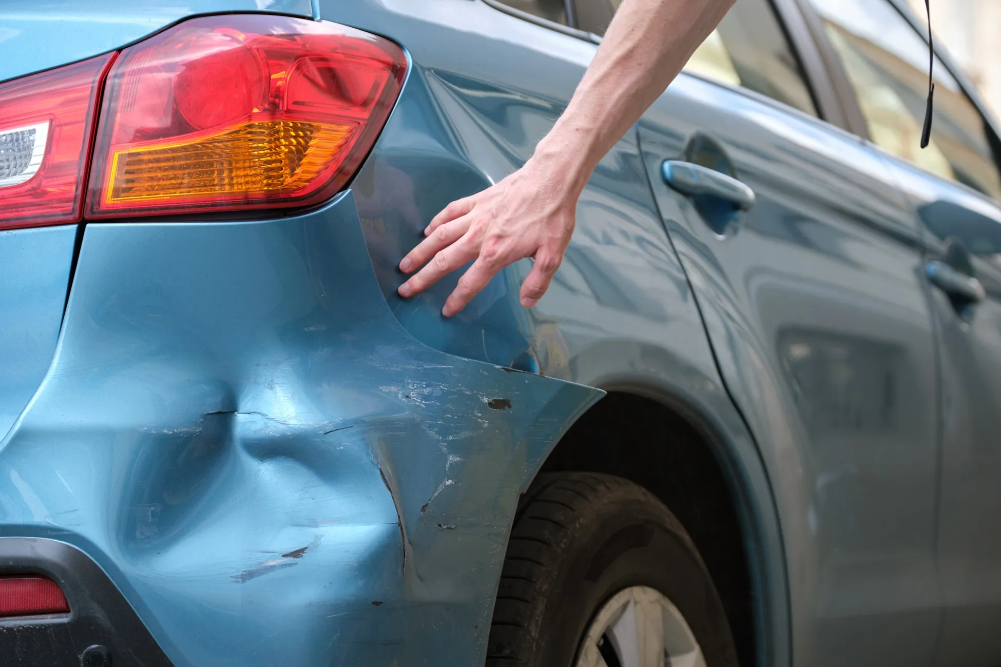 What to do after a hit-and-run accident in San Antonio 1 Driver inspecting dented rear bumper damage after a hit-and-run accident on a city street