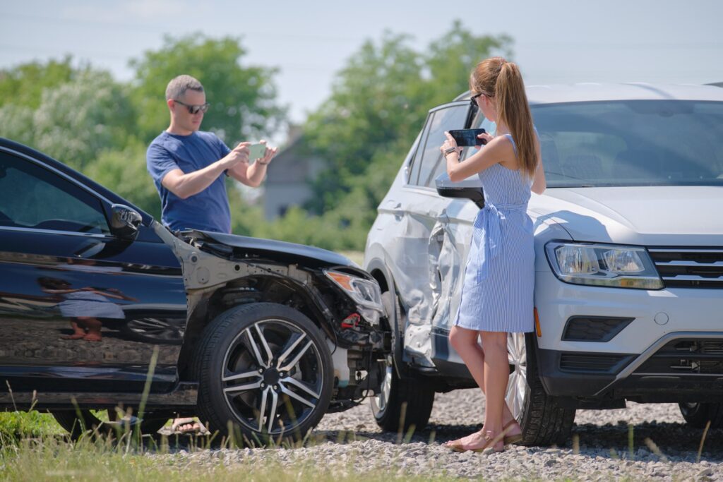 Dos conductores se encuentran junto a sus vehículos accidentados tras una colisión; ambos están fotografiando el lugar del accidente con sus teléfonos móviles para recabar pruebas.