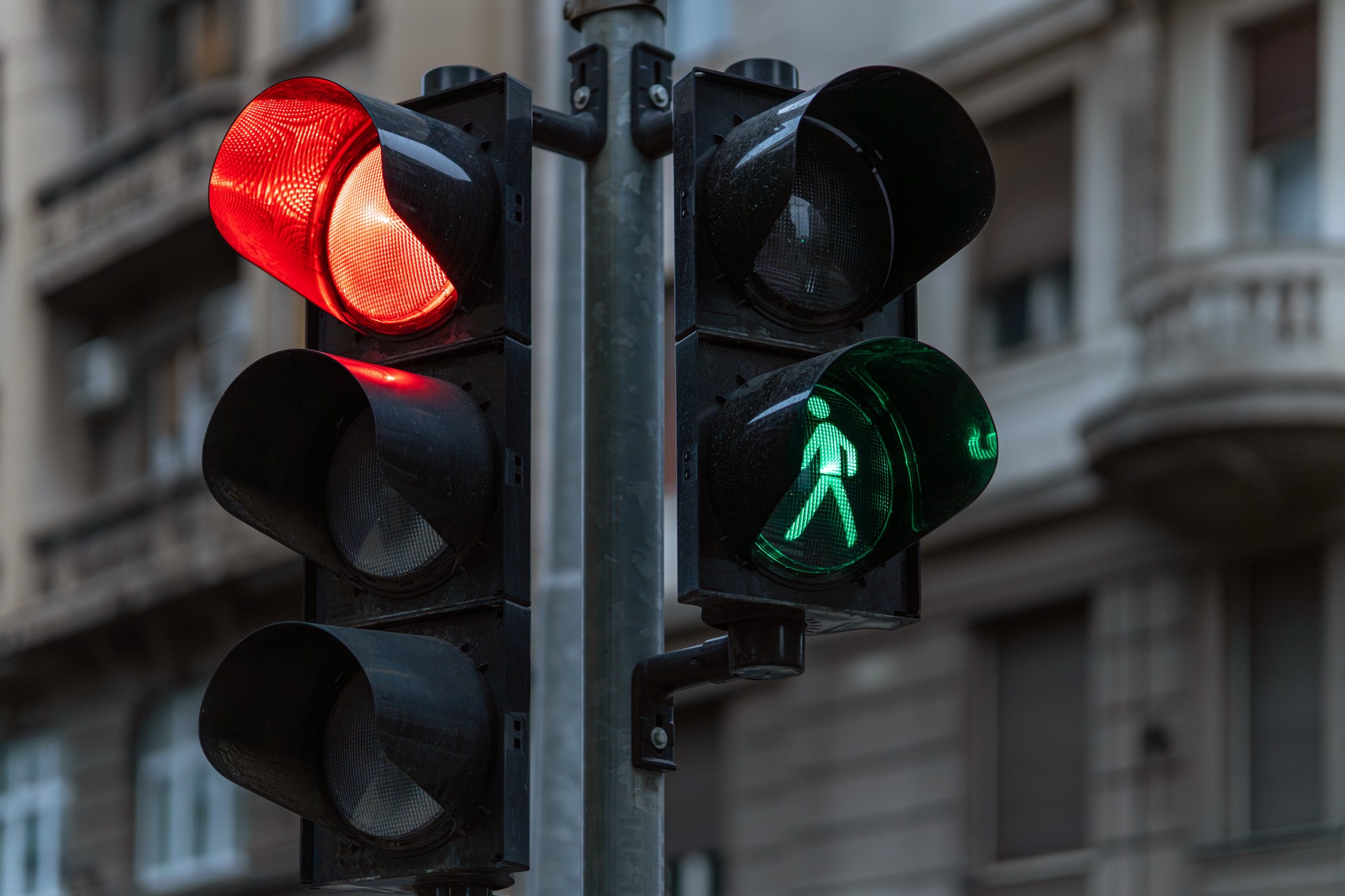 Red vehicle traffic signal beside green pedestrian walk light at urban intersection