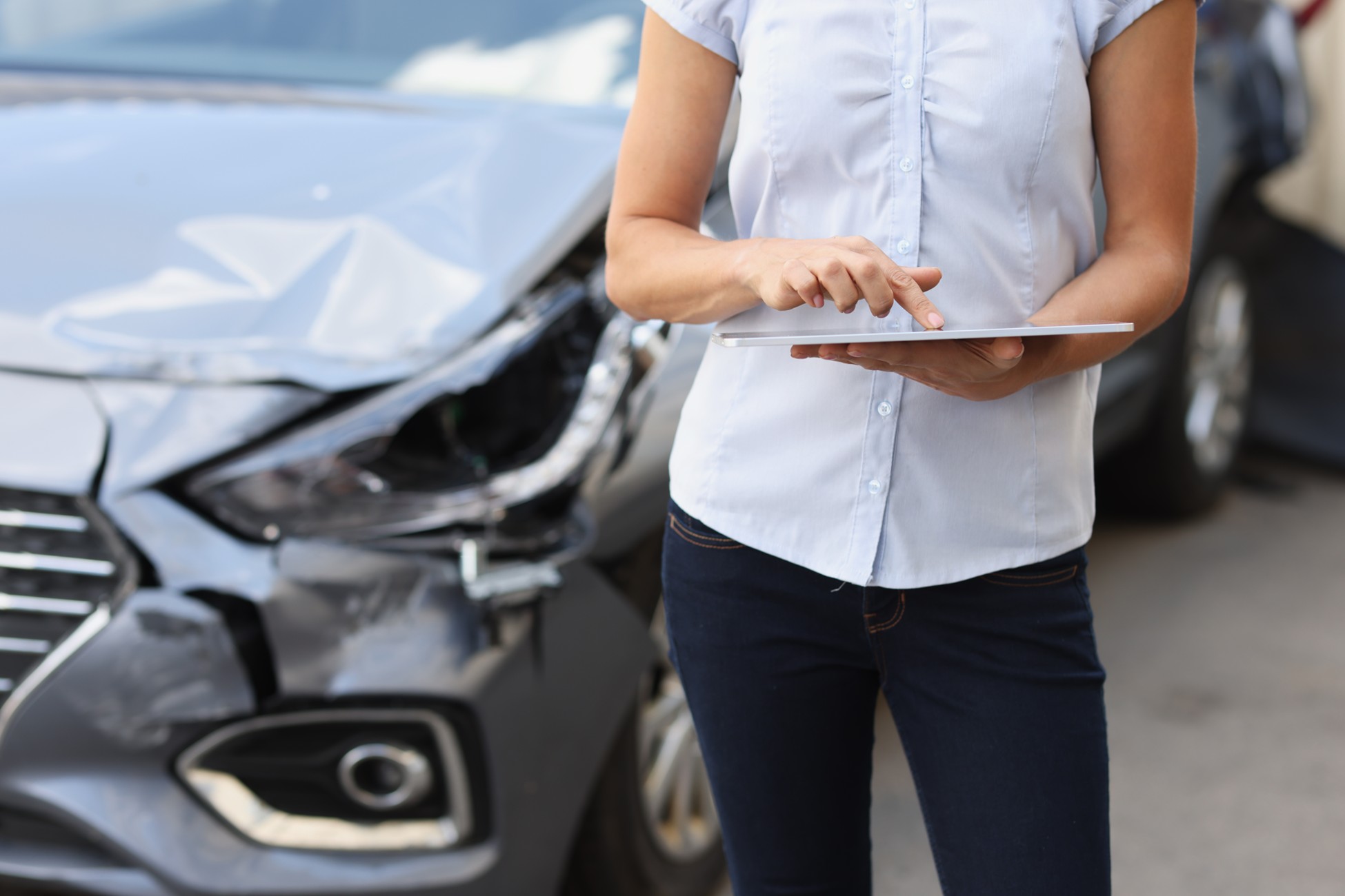 Woman documenting front-end damage to her vehicle on a tablet after a car accident