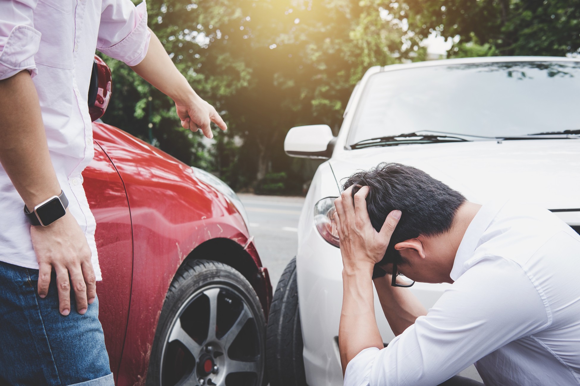 Driver pointing accusingly at distressed man holding his head beside two damaged cars after a collision