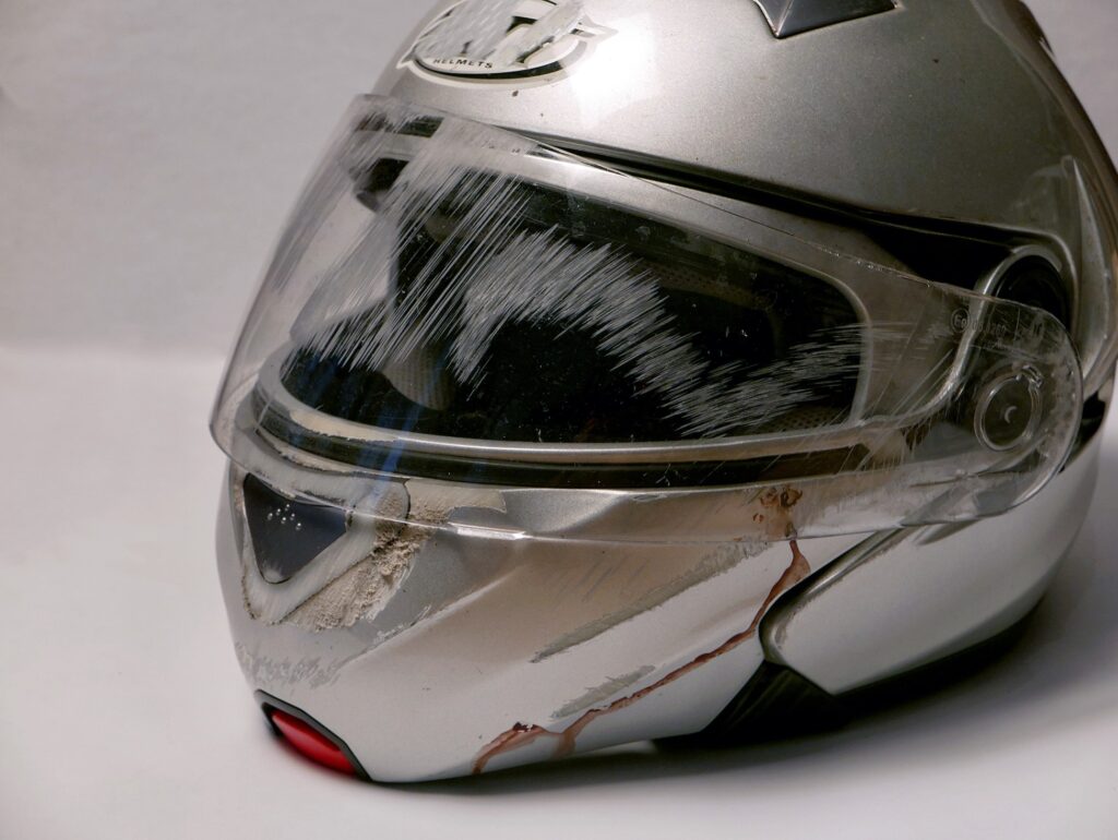 Damaged silver motorcycle helmet showing impact abrasions, cracked visor, and blood residue from a crash