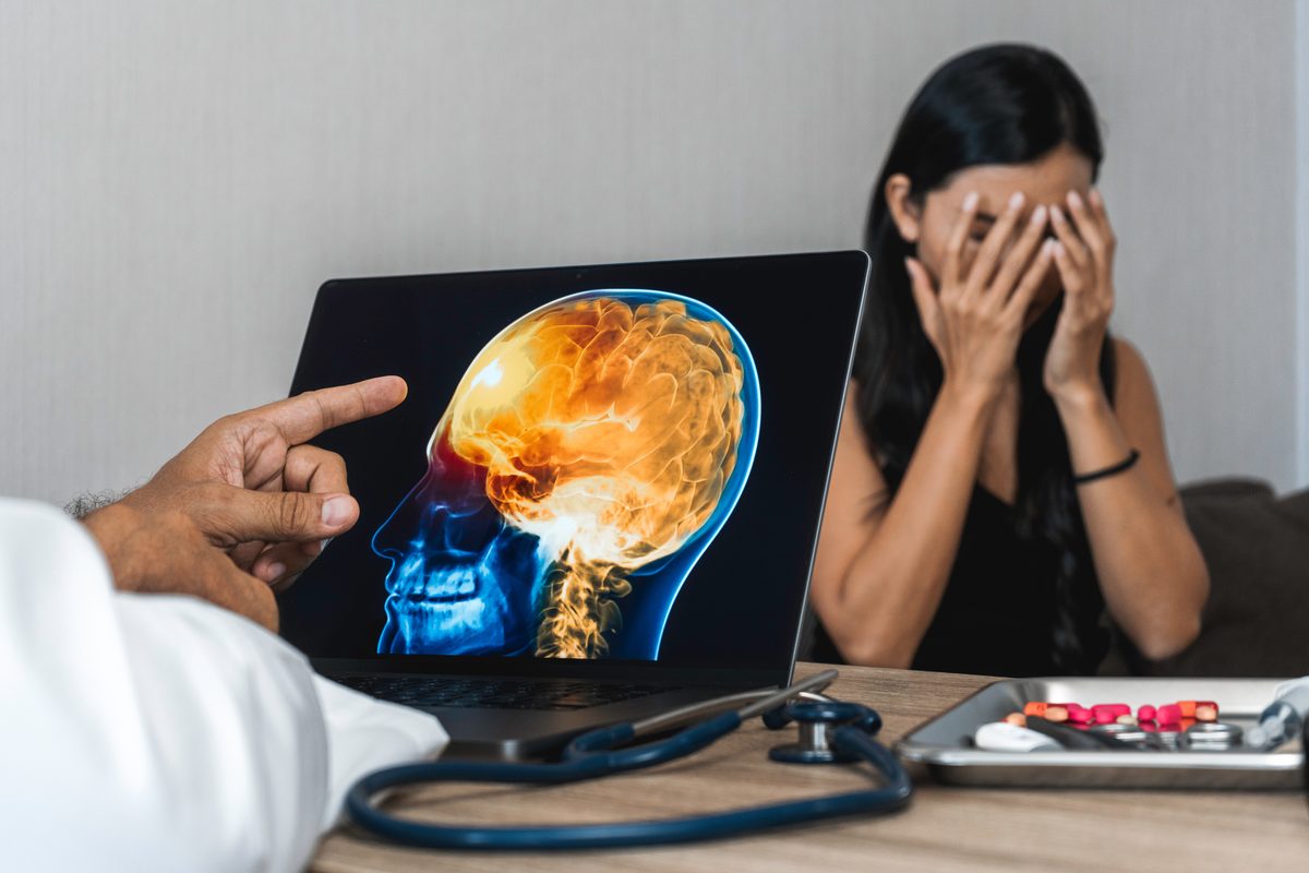 Doctor pointing to a colorful brain scan on a laptop while a distressed patient sits nearby