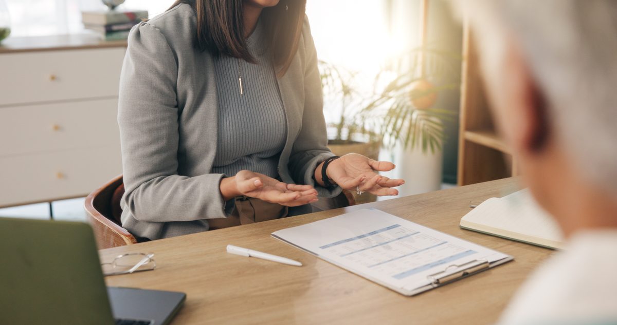 Insurance professional explaining a policy document to a client across a desk, discussing coverage options like PIP
