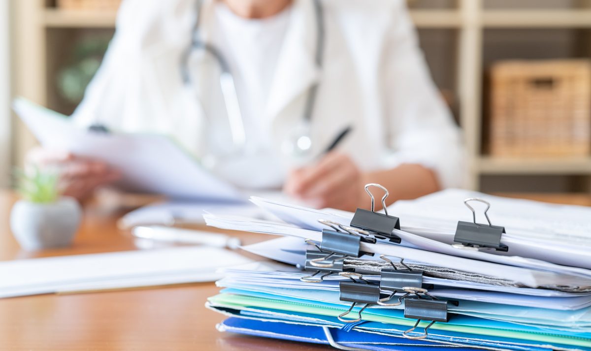 Doctor reviewing a stack of clipped medical bills and paperwork, the kind of expenses PIP coverage can help pay after a crash