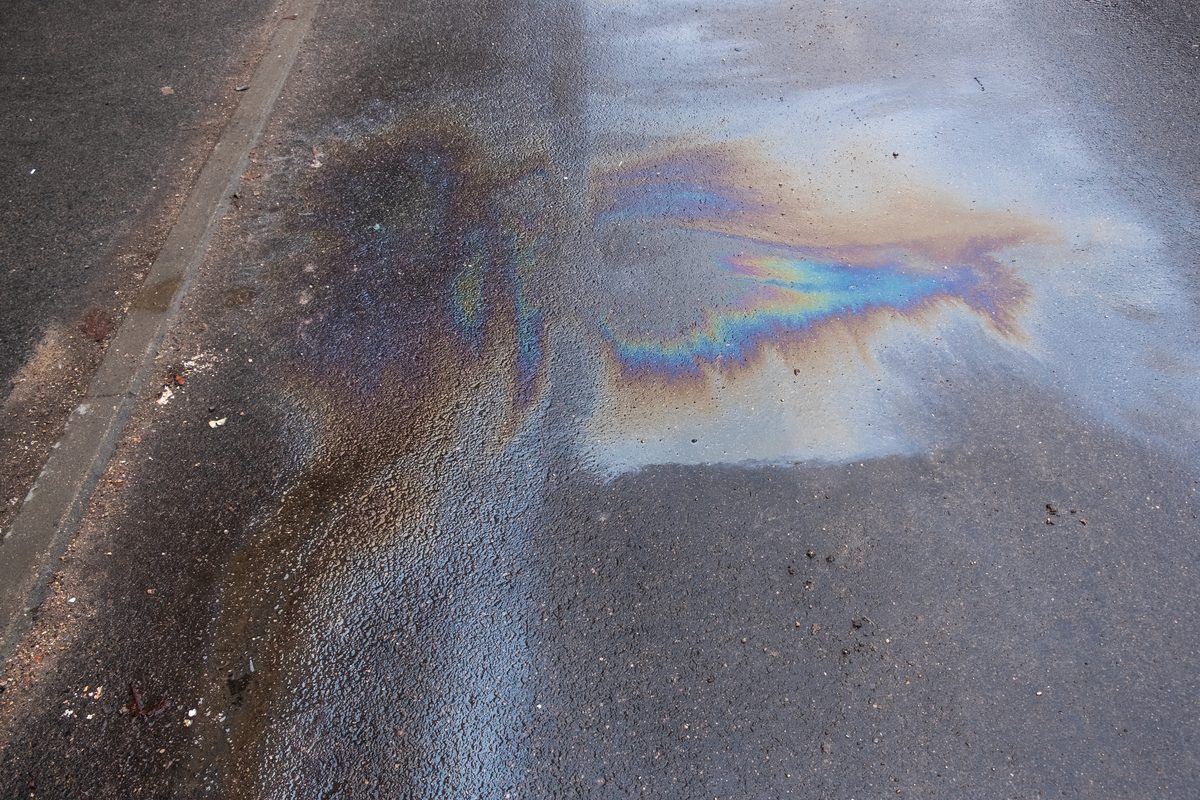 Rainbow sheen of a motor oil slick spread across an asphalt road, like the spill that caused the client’s crash
