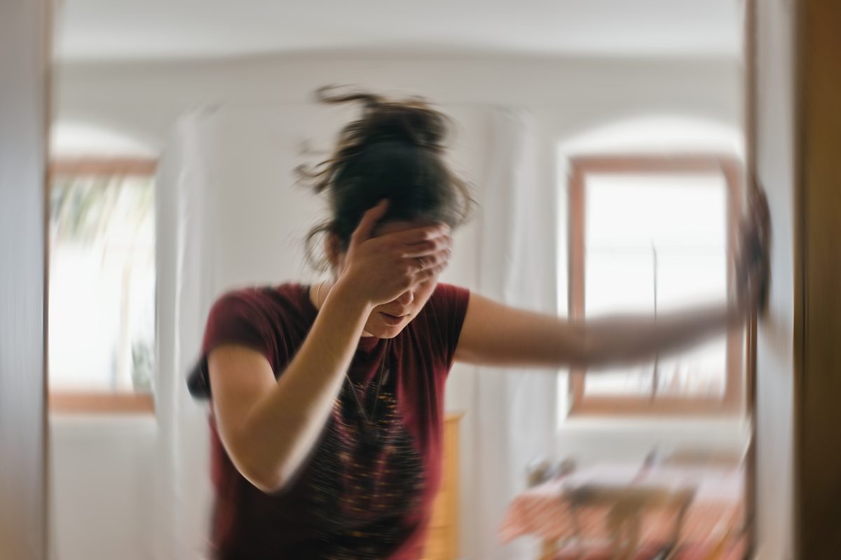 Woman holding her head amid motion blur at home, illustrating dizziness and headaches after a mild traumatic brain injury