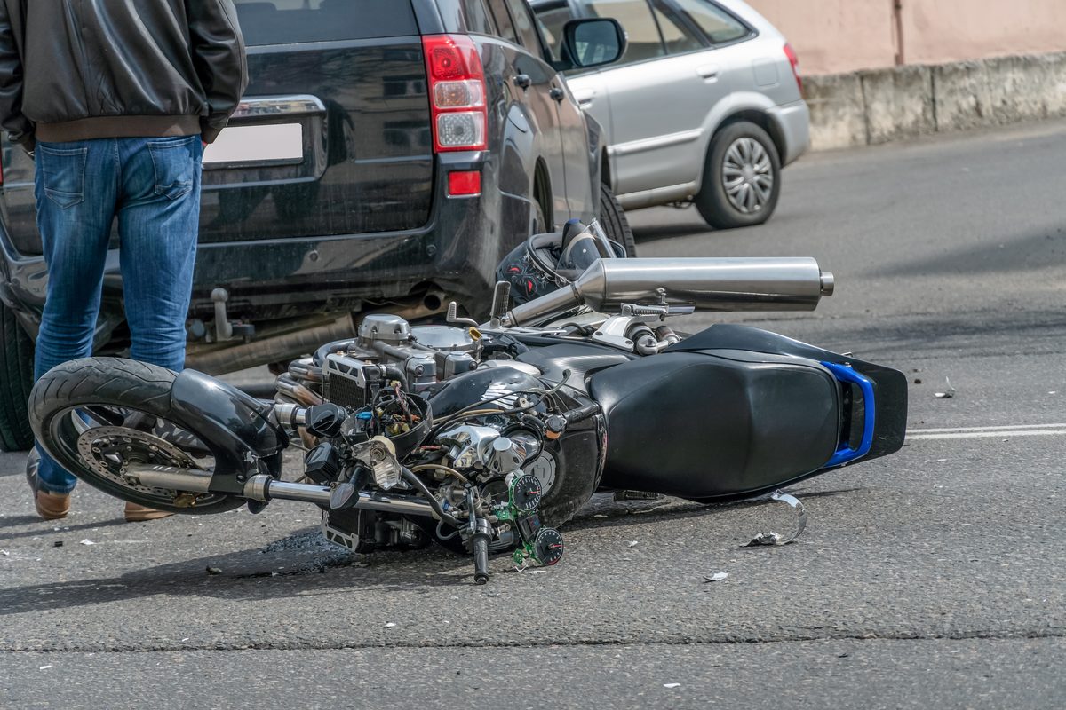 A broken motorcycle lying beside a car after an accident on a city road