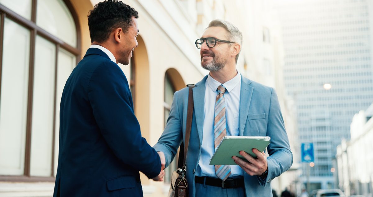 A lawyer holding a folder shakes hands with a client outside an office building