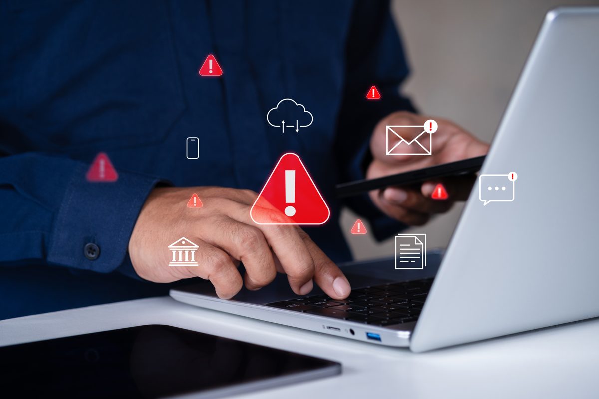 A person typing on a laptop and holding a phone as red warning alerts signal a possible online scam