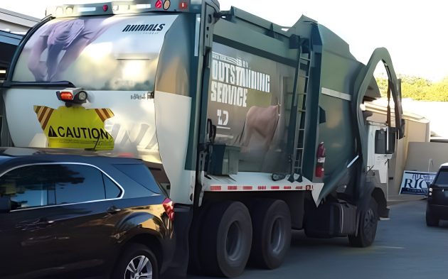 Front-load garbage truck stopped directly behind a dark SUV in a junior high school’s circular drop-off drive